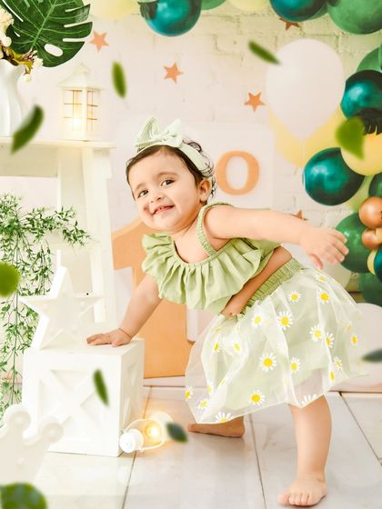 A playful moment during her first birthday shoot. The falling leaves add a touch of magic to this nature-inspired green daisy theme.