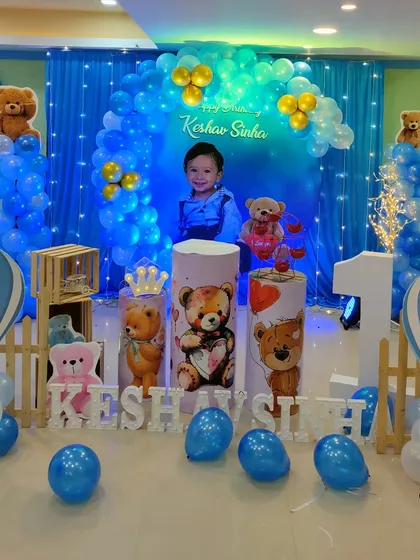 A teddy bear theme with a deep blue backdrop and balloon arch. The setup includes hot air balloon props and fairy lights for a magical touch.