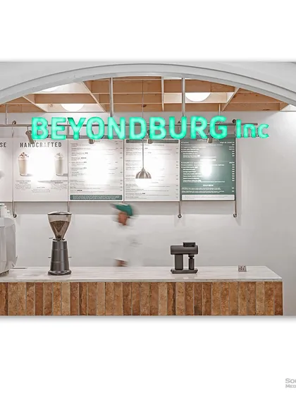 The counter of "Beyondburg Inc," with a motion-blurred figure adding a sense of life and activity. The bright neon sign and clean menu boards create a fresh and modern vibe.