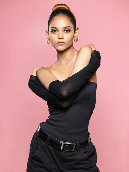 A powerful portrait of a model in a black top and cargo pants, posing against a solid pink background.