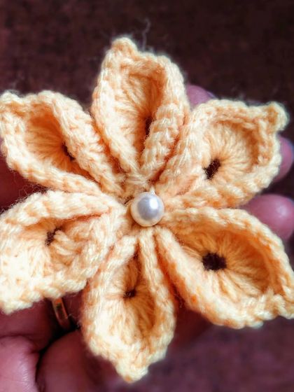 A delicate, hand-held crochet flower with a pearl center. I am always working on new flower designs.