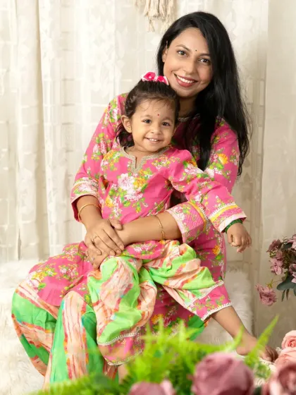 A mother and daughter in matching pink and green traditional outfits smile for a happy portrait together.