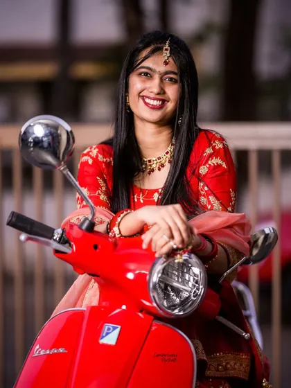 A happy bride leans on her Vespa, her red lehenga beautifully complementing the scooter. This shot is all about joy and personality.