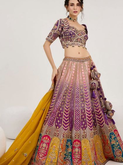 A professional studio shot of a multi-color lehenga with a purple embroidered blouse and a contrasting yellow dupatta. This is a bold and stylish choice for a bride or bridesmaid.
