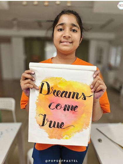 "Dreams Come True." A young participant proudly holds up her inspirational artwork, combining a warm watercolor background with her new lettering skills.