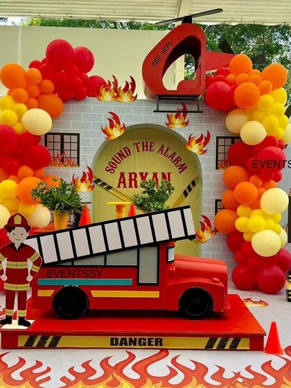 "Sound the alarm!" This firetruck-themed 4th birthday party features a large firetruck prop as the centerpiece. The backdrop is a brick building with balloon "flames," creating a fun and heroic scene.