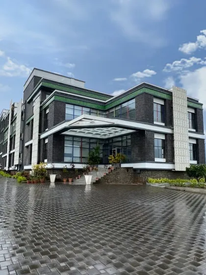 The entrance of Venkateshwar World School in Pune after a rain shower. The wet cobblestones reflect the building's facade, highlighting the material palette of grey stone, white GRC jalis, and green accents.