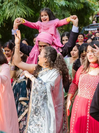 A heartwarming moment of a young flower girl holding a sign that says "Here Comes My Bua," leading the baraat.