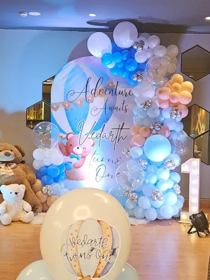 A full view of a vibrant 'Adventure Awaits' first birthday party. This hot air balloon and teddy bear theme shows our detailed work with custom backdrops, elaborate balloon garlands, and marquee lighting.