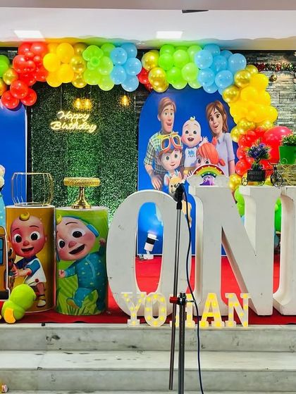 A Cocomelon party on a stage, featuring large 'ONE' letters and the iconic yellow school bus cutout.