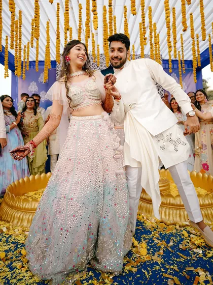 A moment of pure fun on the dance floor. The couple is captured mid-dance during their Sangeet, surrounded by yellow flower petals and smiling guests.