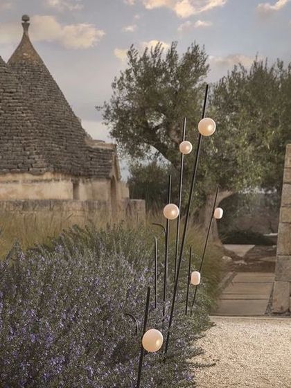 The Firefly outdoor lights are placed along a gravel path in an Italian-style garden, providing gentle, atmospheric wayfinding light.