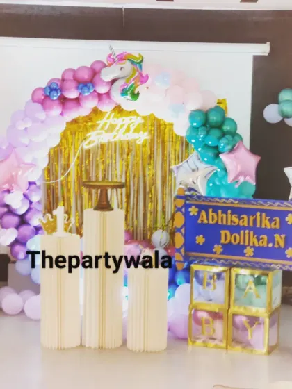 This unicorn theme features a gold shimmer backdrop behind the balloon arch. The mix of pastel and teal balloons with unicorn cutouts creates a very magical and sparkly effect.