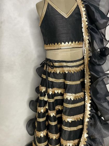 A chic and modern black and gold lehenga, perfect for a sangeet or reception. The design features a striped skirt and a dramatic ruffled dupatta for a high-fashion look.