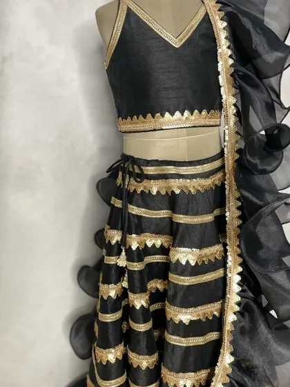 A chic and modern black and gold lehenga, perfect for a sangeet or reception. The design features a striped skirt and a dramatic ruffled dupatta for a high-fashion look.