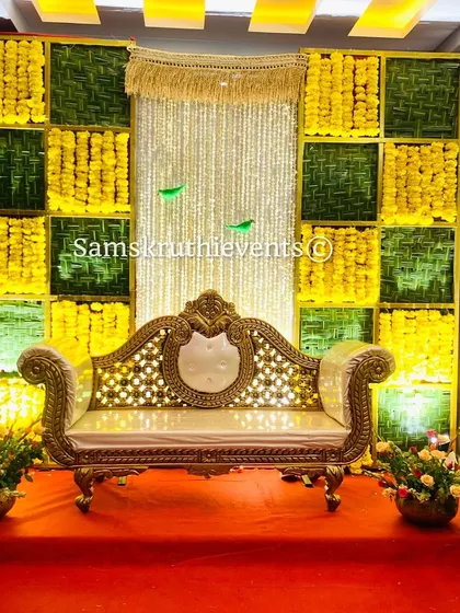 A vibrant checkerboard backdrop with a central panel of hanging jasmine strings. The combination of yellow marigolds and woven green leaves is illuminated to create a warm and festive glow.