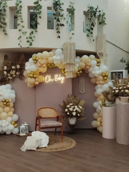 A wider shot of the boho baby shower decor, showing the full balloon arch and the cozy seating area with a jute rug and wooden chair.