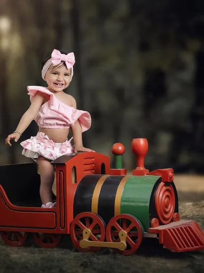 A big, happy smile from this little passenger. The lush green background makes the colors of the toy train pop in this fun outdoor shot.