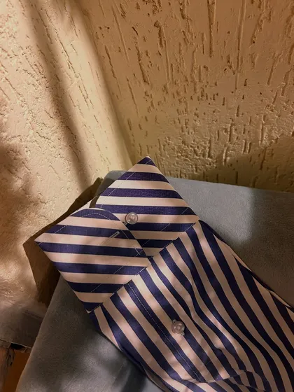 A detail shot of the cuff on the striped cotton shirt. The pattern is perfectly matched, a hallmark of high-quality tailoring.