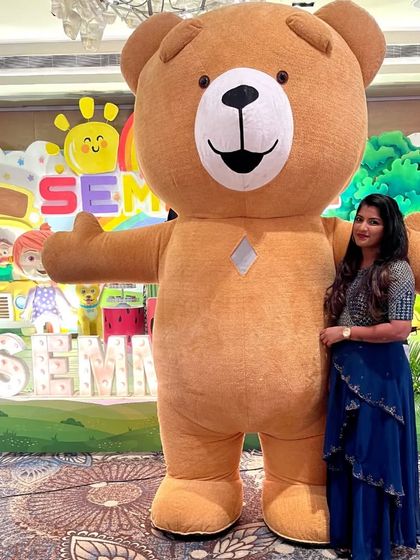 A guest poses next to our giant brown Teddy Bear, showing its impressive size. It's a fantastic centerpiece for photos at any celebration.