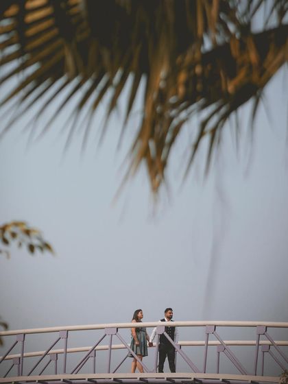 A wide shot of a couple on a bridge, framed by palm leaves, creating a sense of scale and a beautiful composition.
