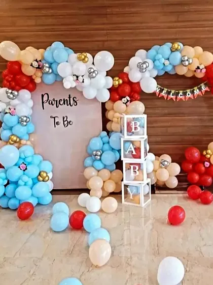 A playful 'Parents To Be' baby shower decoration. The balloon arch uses primary colors like red and blue, with 'BABY' blocks and other fun elements.