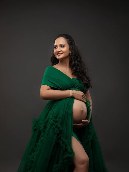 A three-quarter portrait in the green gown, showcasing its rich color and texture. The soft lighting highlights her joyful expression and the beautiful curves of pregnancy.