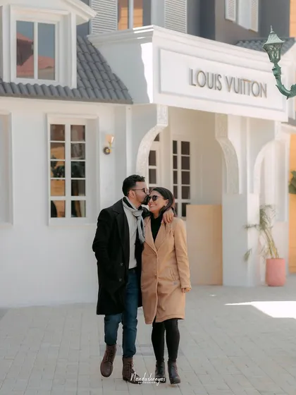 A sweet moment as the groom kisses his bride's head while they walk down a European-style street set.