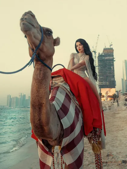 Where the desert kisses the beach. A unique low-angle shot of a model on a camel, with the modern Dubai skyline rising in the background.