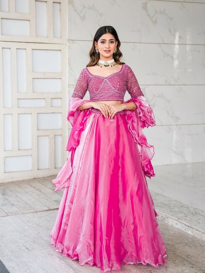 A classic pose in our rose pink lehenga. The combination of the sparkling blouse, organza skirt, and ruffled sleeves creates a look that is both modern and unforgettable.