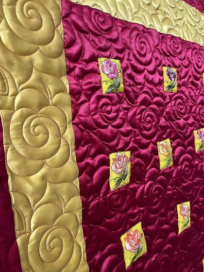A close-up of a luxurious quilt made with silk fabric, featuring large, swirling rose motifs created with our longarm machine.