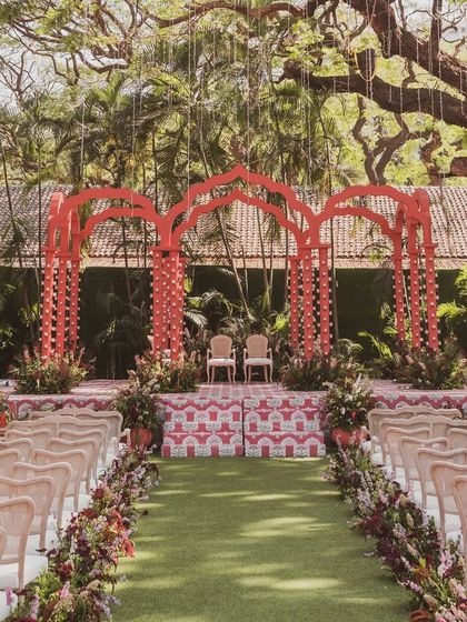 The view down the aisle towards the 'Gulal Bagh' mandap. The path is lined with flowers, leading guests' eyes to the stunning red structure under a massive tree.