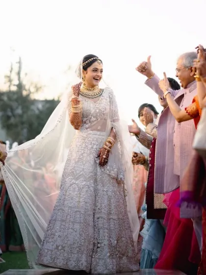 The bride's joyful walk down the aisle, with her family cheering her on. Her flowing veil and elegant lehenga made for a stunning sight.