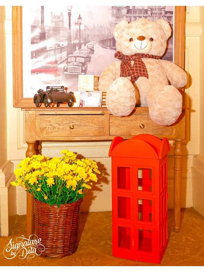 A cozy corner vignette from the London-themed party, featuring a classic teddy bear, a miniature red telephone box, and a framed picture of a London street scene.