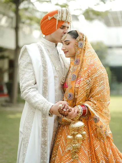 A tender moment between the couple. The groom's kiss on her forehead is a classic expression of love. I styled their outfits to be complementary, with his ivory sherwani providing a perfect balance to her vibrant orange lehenga.