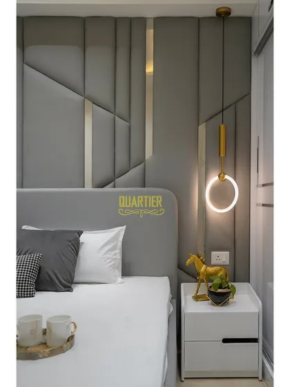 This guest bedroom at Tata LaVida features a sophisticated grey color palette. The full-height quilted headboard with metallic inlays provides a touch of glamour, while the pendant lights add a modern, sculptural element.