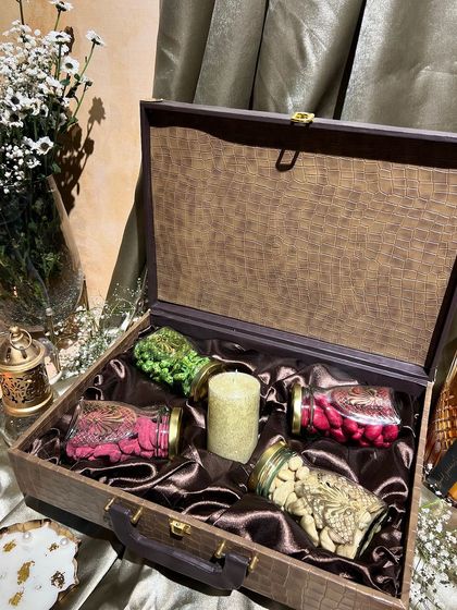 A rustic wooden trunk-style box for Diwali, lined with rich brown satin. It's filled with jars of dry fruits and a candle, perfect for a warm, earthy theme.
