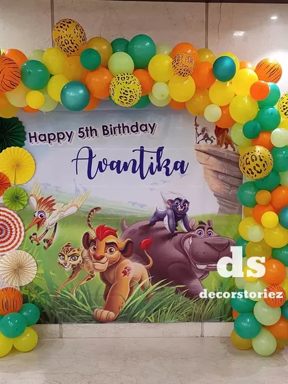 A lively Lion King themed decoration for a 5th birthday party. The setup includes a large, custom-printed backdrop with characters from the movie, framed by a vibrant balloon arch.