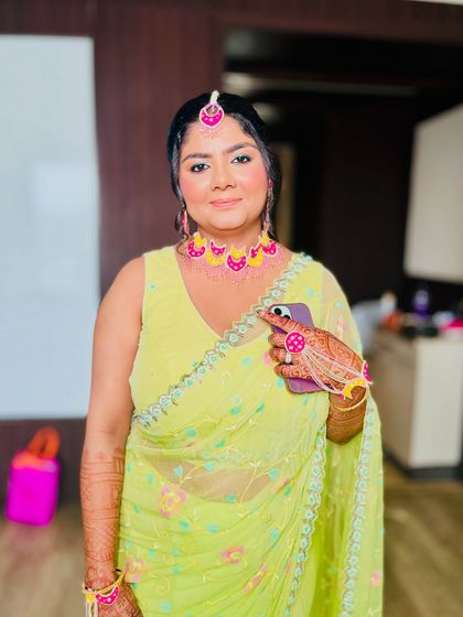 A stunning Haldi look. The lime green saree is paired with pink floral jewelry and a soft, dewy makeup look that makes her skin glow.