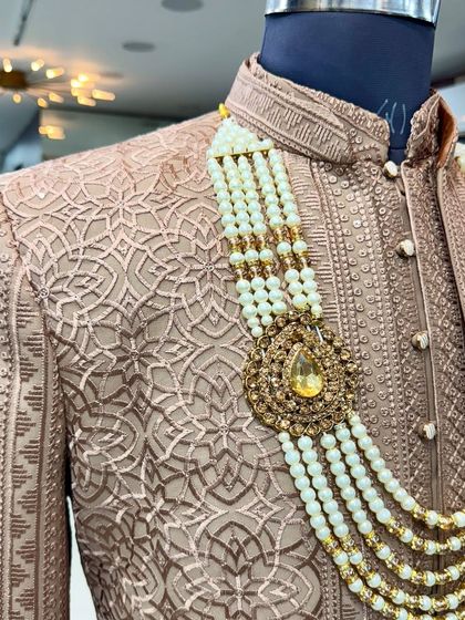 A detailed shot of the groom's accessories on the Mocha Brown Jodhpuri. The large pendant on the pearl necklace adds a touch of grandeur.