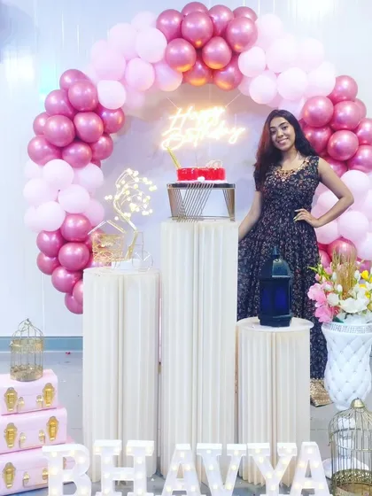 A happy client posing with her pink-themed birthday decor. The balloon arch and plinth setup create the perfect backdrop for birthday photos.