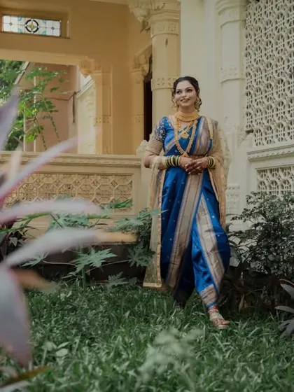 A wider shot of the bride in the same garden setting, framed by plants. This composition gives a sense of place and highlights the full elegance of her traditional attire.
