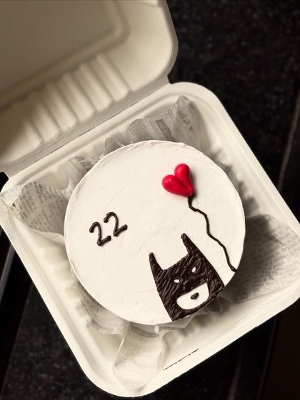 A minimalist and cool Batman-themed bento cake. This design features the Batman symbol holding a red heart-shaped balloon, celebrating a 22nd birthday.