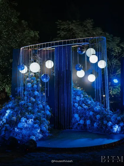 A statement decor piece for a Sangeet, featuring a glowing installation of orbs and light strings surrounded by mounds of blue hydrangeas, creating a captivating, otherworldly photo op.