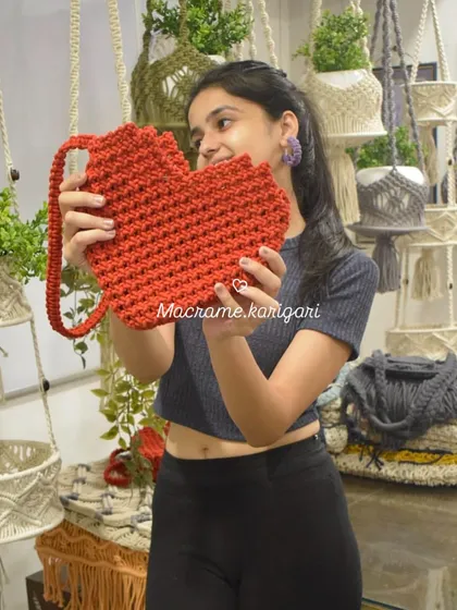 Holding up our bright red, heart-shaped crochet bag. This is a fun and playful design that we absolutely love making. It's a perfect statement piece for Valentine's or any day you want to spread some love.
