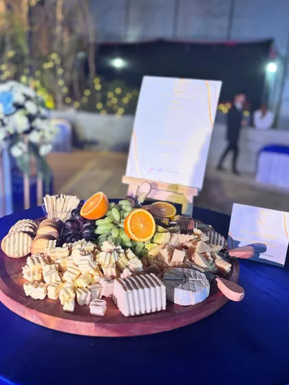 A sophisticated cheese and charcuterie board prepared for a Godrej Properties event. The display includes a mix of local and imported cheeses, crackers, and fresh fruit, with a menu card for guests.