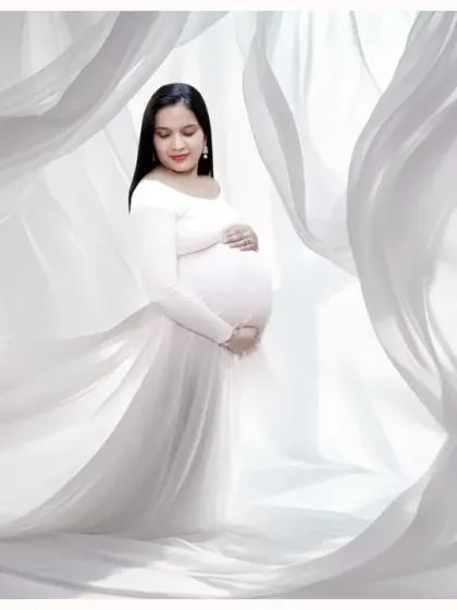An angelic solo portrait in a flowing white gown. The sheer white fabric drapes around the mother-to-be, creating a soft, dreamy, and ethereal look.