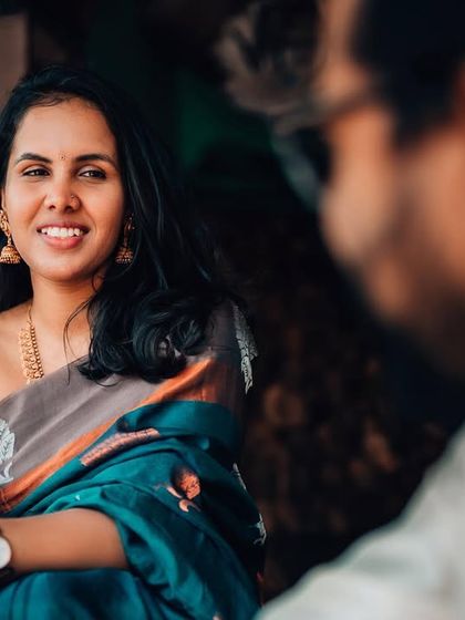 A beautiful candid portrait of a woman in a saree, smiling at her partner in a bustling market. The shallow depth of field brings the focus entirely to her happy expression.