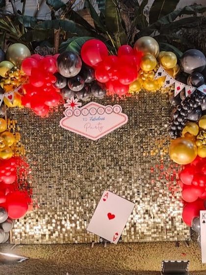 A '50 & Fabulous' party with a casino theme, featuring a gold shimmer wall, a balloon arch in red, black, and gold, and playing card props.