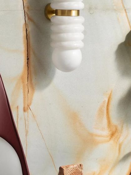 A close-up of the minimalist master retreat, highlighting the unique wall sconce against the marble backdrop. The textures of the maroon bed and grey fabrics add layers of understated elegance.